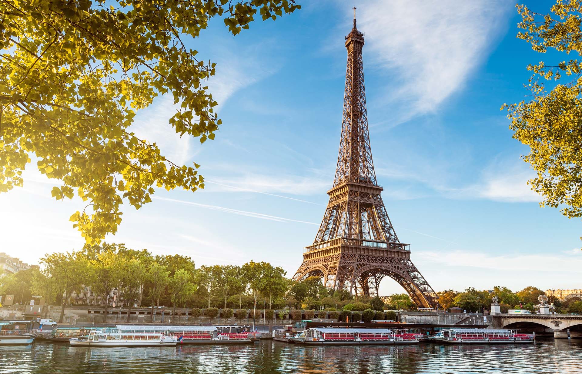 A view of the base of the Eiffel Tower from a river with tour boats on it.