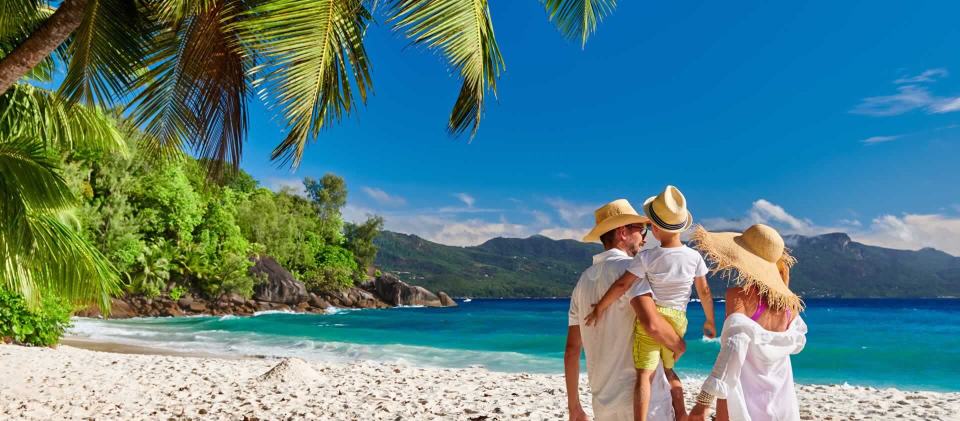A family of 3 standing on a beach with their backs to the camera