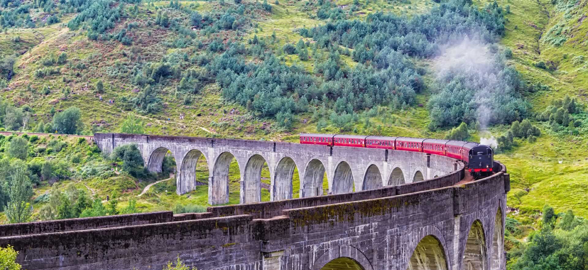 A red train travelling over the Glenfinnan Viaduct